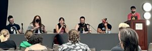 Emily's photo shows four panelists seated at a table and a standing moderator at a podium